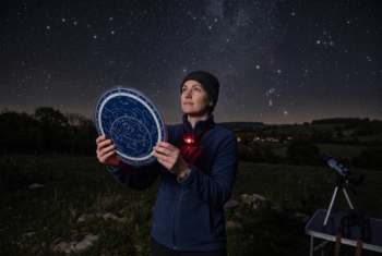 Planisphere being used to identify constellations under a star-filled night sky